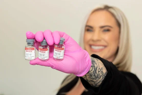Revitalize Your Look with Jeuveau Smiling aesthetic professional holding three vials of Jeuveau, wearing pink gloves.